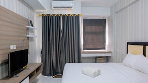 Une chambre d’hôtel avec un lit, un téléviseur posé sur un meuble en bois, une fenêtre avec des rideaux et un appareil de climatisation.