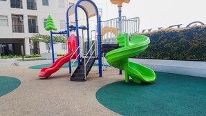 Une aire de jeux avec deux toboggans et une structure d’escalade, entourée d’un espace paysager avec un bâtiment en arrière-plan.