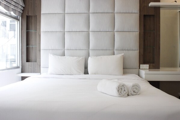 Una cama bien hecha con sábanas y almohadas blancas, un ventanal con cortinas y un cabecero moderno.