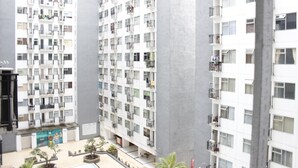 Un immeuble résidentiel à plusieurs étages doté de balcons, d’une cour intérieure agrémentée de plantes en pot et d’une fresque murale sur le niveau inférieur.