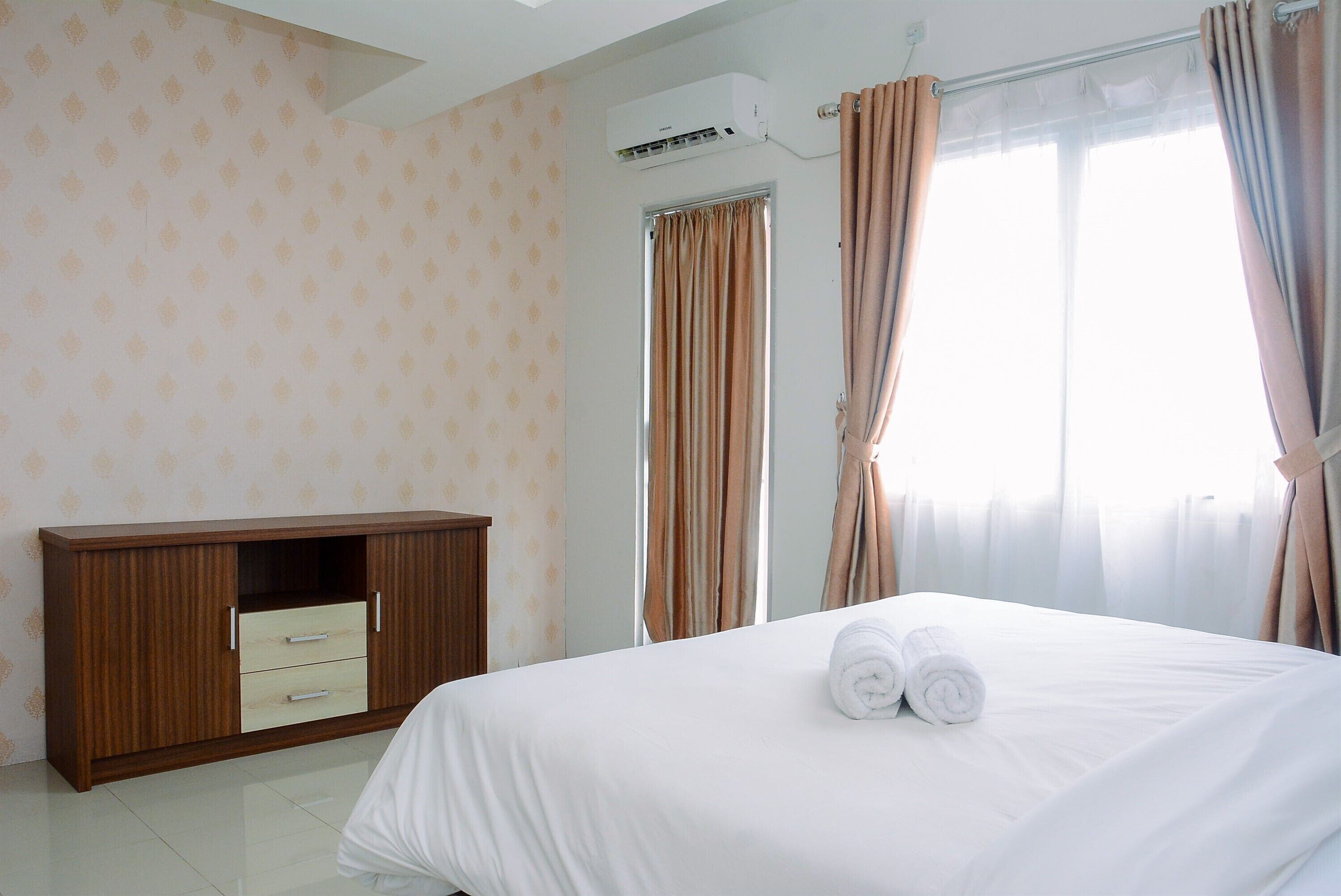 A hotel room with a bed, a wooden wardrobe, and a window with curtains.