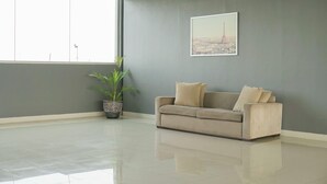 A spacious room with a large window, a grey wall, a framed picture, a beige sofa, and a potted plant. - 2BR Apartment at Park View Condominium near Universitas Indonesia (Depok)
