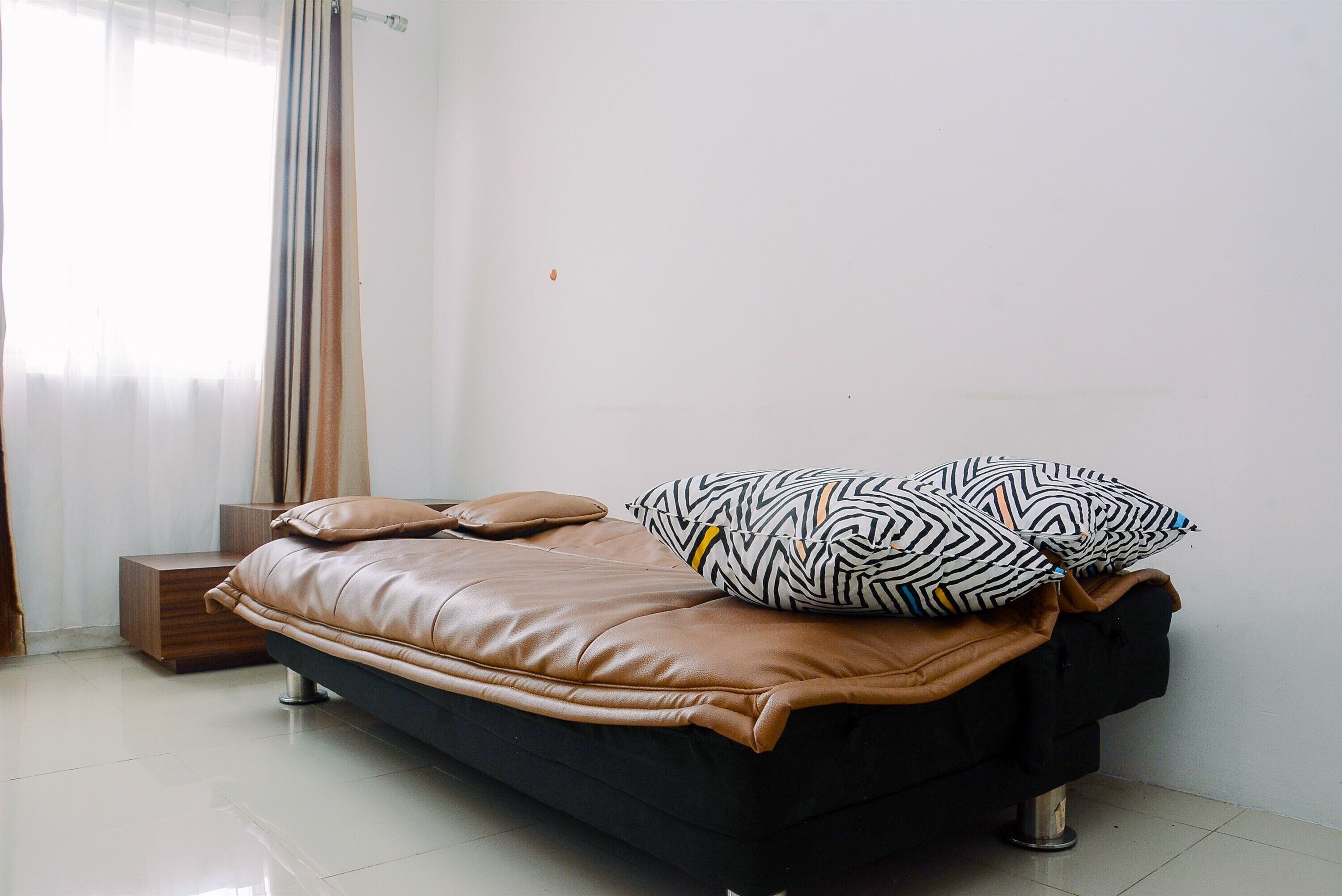 A modern bed with a black frame and brown bedding, a wooden nightstand, and a window with sheer curtains.