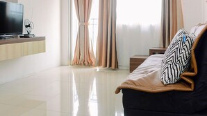 A modern living room with a flat-screen TV, a sofa with patterned cushions, and a large window with curtains. - 2BR Apartment at Park View Condominium near Universitas Indonesia (Depok)