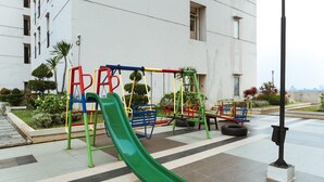 An outdoor playground with a green slide, swings, and climbing structures.