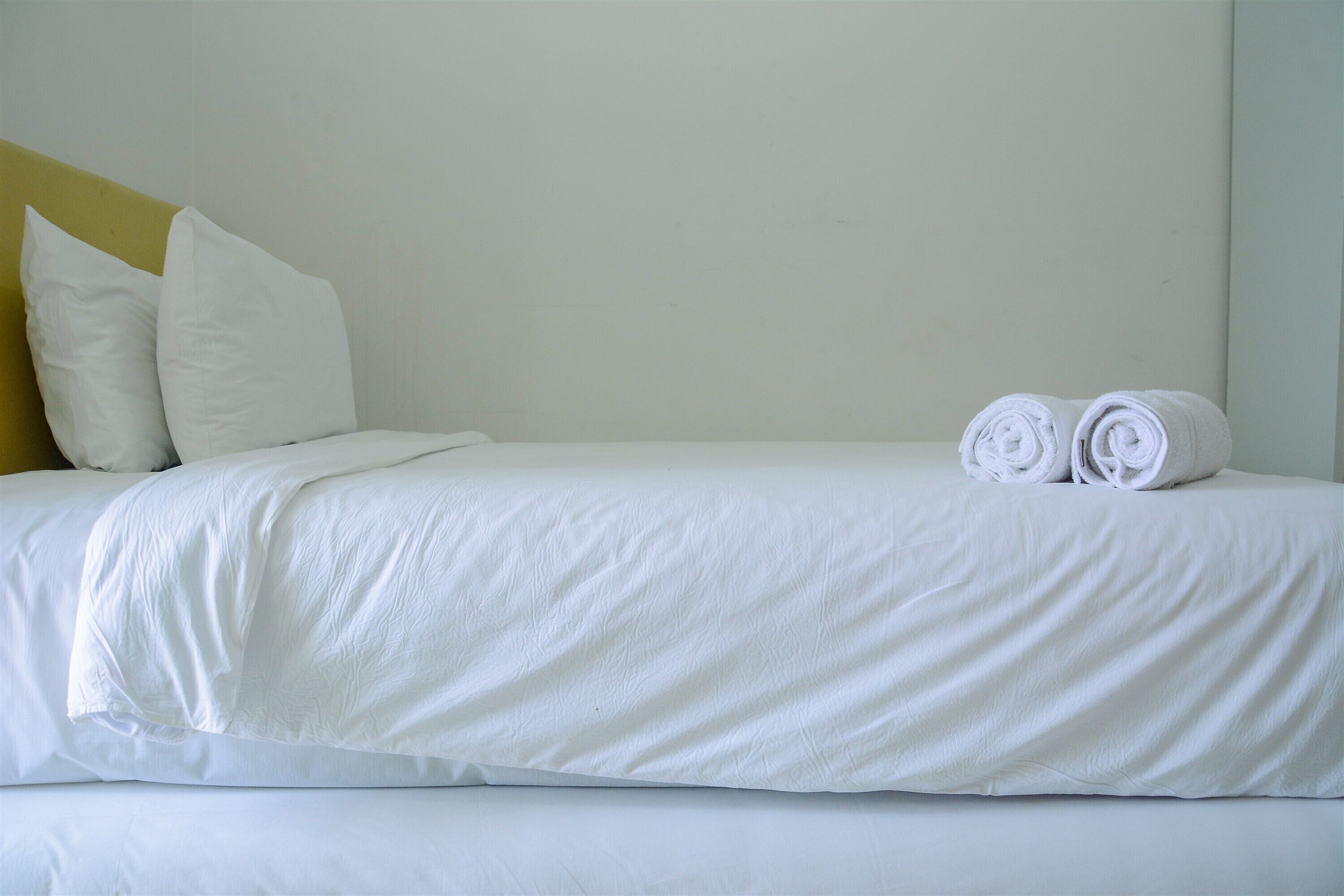Ein ordentlich bezogenes Bett mit weißen Leinen und Kissen, ein aufgerolltes Handtuch auf dem Bett und ein gelber Bettrahmen.