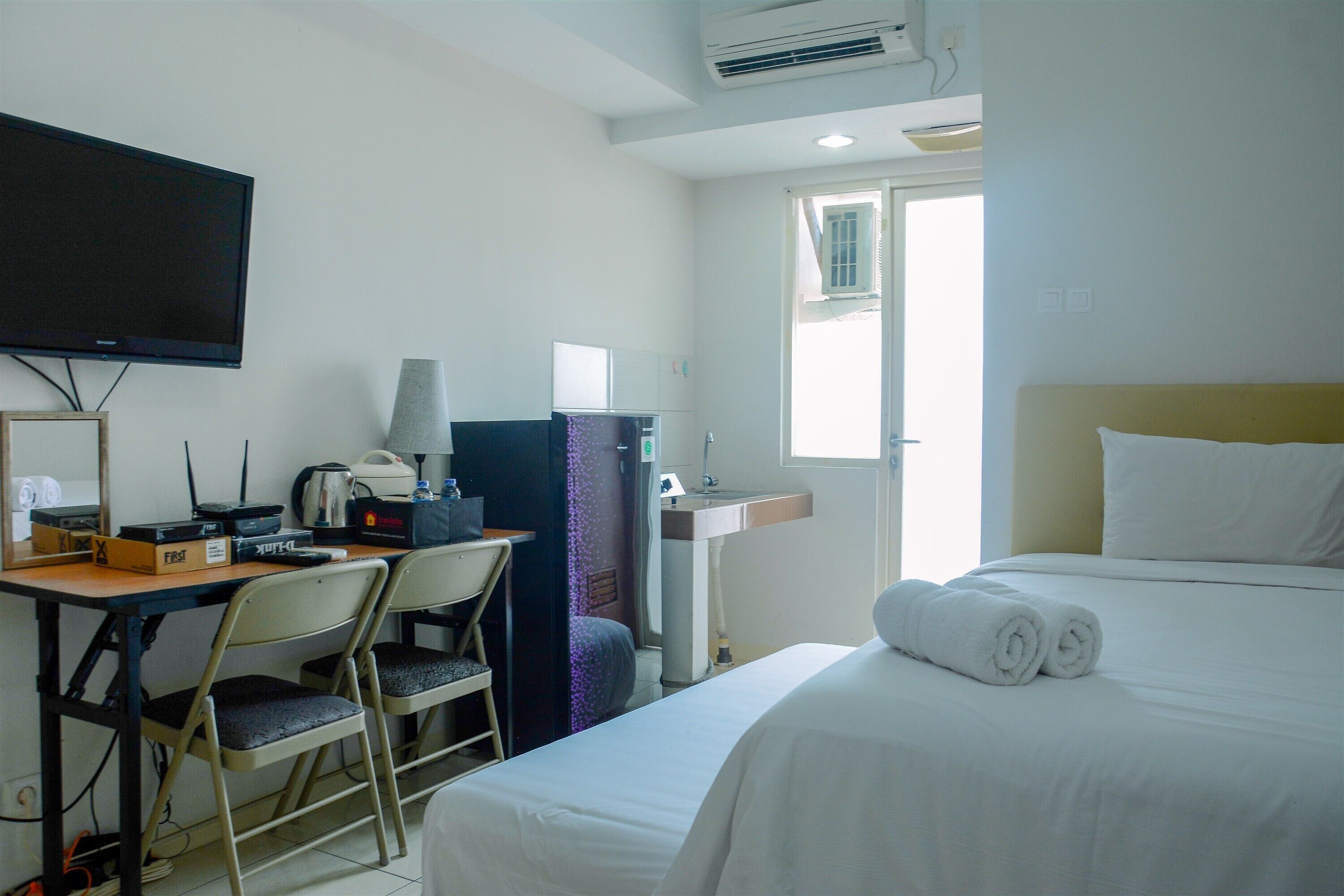 Una habitación de hotel con cama, escritorio, computadora, televisor y ventana.