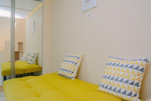 A room with a yellow bed, two pillows with a geometric pattern, a mirror, and a small whiteboard on the wall.