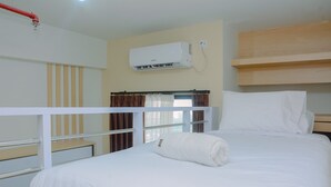 A hotel room with a bed, a window with curtains, a wall-mounted air conditioner, and a wooden shelf above the bed. - Stylish and Convenient Studio Dave Apartment (Depok)