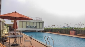A rooftop pool area with a wooden deck, lounge chairs, and a table with chairs. - Stylish and Convenient Studio Dave Apartment (Depok)