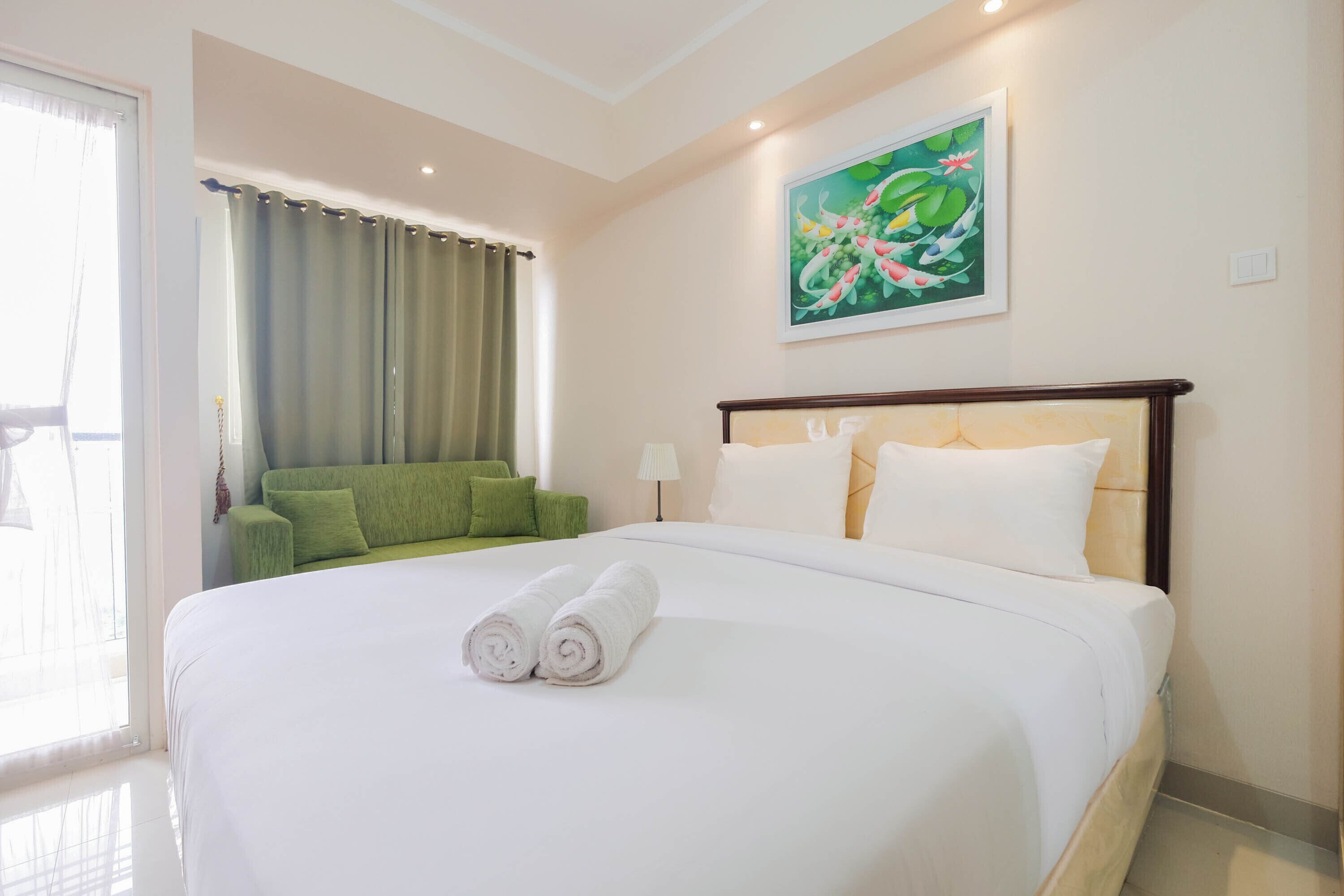Een hotelkamer met een groot bed, een groene bank, een schilderij aan de muur en een raam met gordijnen.