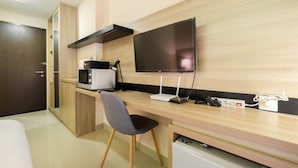 Quarto de hotel moderno com escrivaninha de madeira, televisão de tela plana, micro-ondas e mini-geladeira.