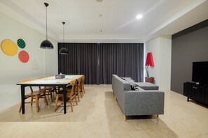 Una sala de estar moderna con un sofá gris, una mesa de comedor de madera con sillas, un mueble negro para televisor y un ventanal con cortinas.