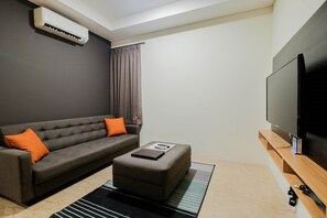 A modern living room with a grey sofa, ottoman, and a flat-screen TV mounted on the wall. - 1BR Pancoran L'Avenue Comfy Apartment (Jakarta)