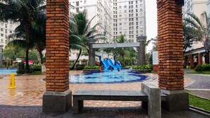 A swimming pool with a water slide, surrounded by palm trees and brick pillars. - Big and Cozy 3BR Apartment Green Palace Kalibata (Jakarta)