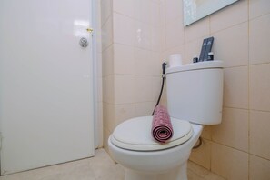 A white toilet with a pink towel on the seat, a toilet paper holder, and a wall-mounted sign. - Big and Cozy 3BR Apartment Green Palace Kalibata (Jakarta)