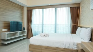 A modern hotel room with a large bed, a flat-screen TV, and a view of the city through large windows. - Cozy Studio Apartment at Nine Residence connected to Mall (Jakarta)