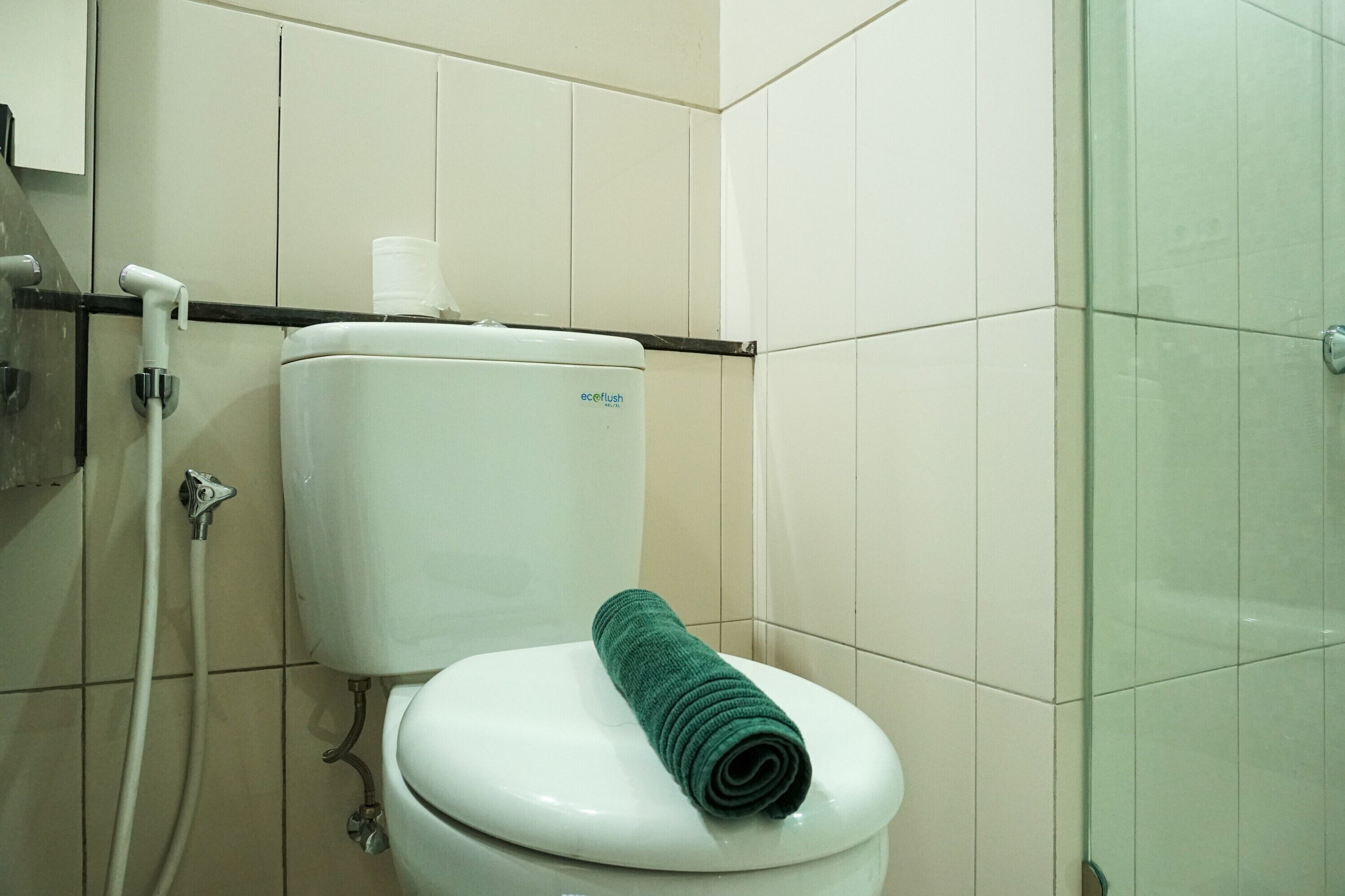 A bathroom with a white toilet, a green towel, and a glass shower enclosure.