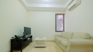 A living room with a beige sofa, a black entertainment unit, a white coffee table, and a window with a view of a building. - Relaxing 1BR Apartment at L'Avenue Pancoran (Jakarta)