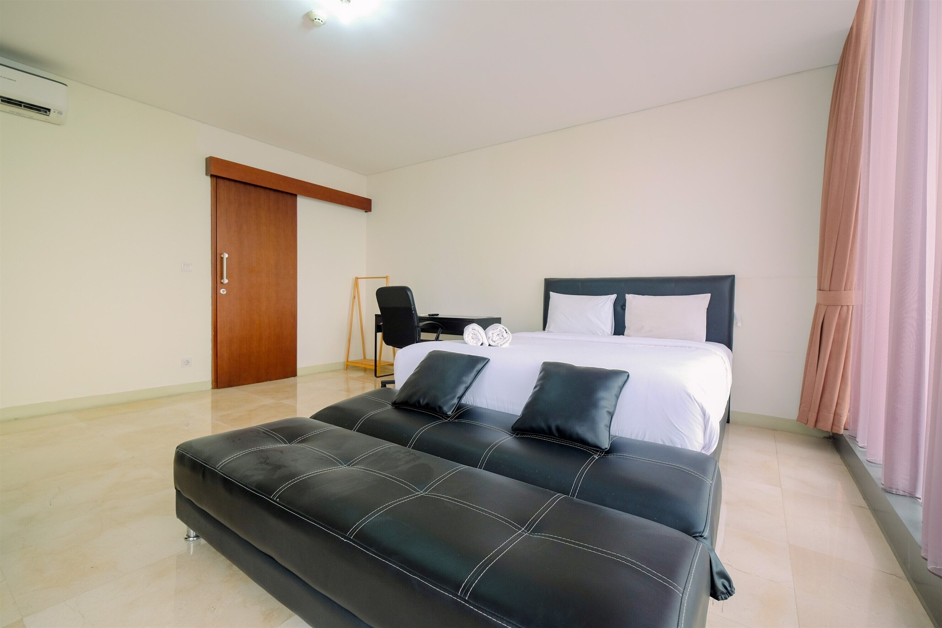 A hotel room with a large bed, a black leather sofa, a desk with a chair, and a wooden door.