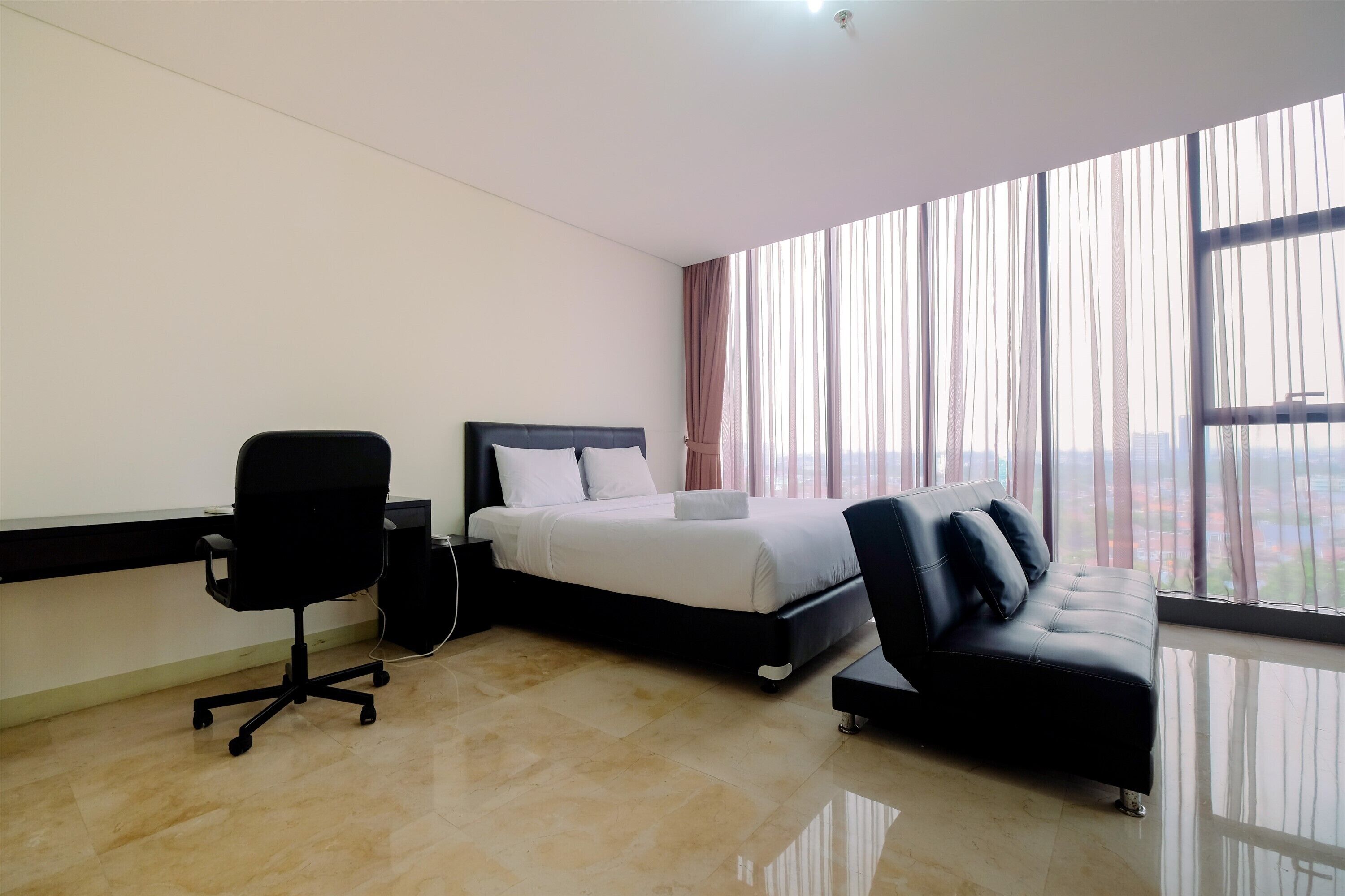 A modern hotel room with a bed, a black office chair, a black sofa, and large windows offering a city view.