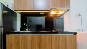 A modern kitchen with wooden cabinets, a stainless steel refrigerator, a built-in oven, and a sink with a faucet. - Relaxing 1BR Apartment at L'Avenue Pancoran (Jakarta)