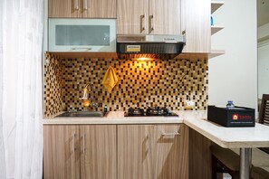 A modern kitchen with wooden cabinets, a microwave, a stove, and a tiled backsplash. - Cozy and Homey 2BR at Kalibata City Apartment (Jakarta)