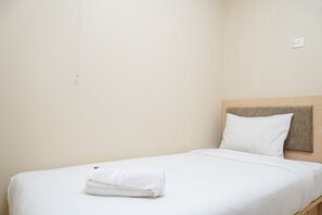 A single bed with a wooden headboard, white bedding, and a folded white towel on the bed. - Cozy and Homey 2BR at Kalibata City Apartment (Jakarta)