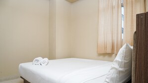 A neatly made bed with white linens and two rolled towels, a wooden wardrobe, and a window with checkered curtains. - Cozy and Homey 2BR at Kalibata City Apartment (Jakarta)