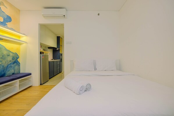 A hotel room with a bed, a seating area with a bench, and a kitchen visible through an open doorway. - Comfortable Studio Apartment at Woodland Park Residence (Jakarta)