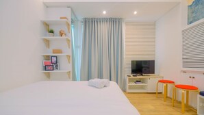 Ein modernes Hotelzimmer mit einem Bett, einem Schreibtisch mit Computer, zwei roten Hocker und einem Fernseher.