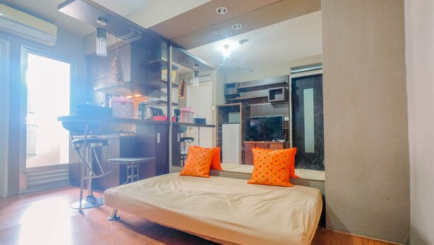 A modern bedroom with a bed, orange pillows, a desk, and a television. - Strategic 2BR at Kalibata City Apartment (Jakarta)