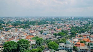A cityscape with a prominent green-domed building in the foreground, surrounded by residential areas and various buildings. - Strategic 2BR at Kalibata City Apartment (Jakarta)