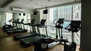 A gym with treadmills, elliptical machines, and a large window with a city view. - 1BR Apartment with Study Room at Gallery West Residence (Jakarta)