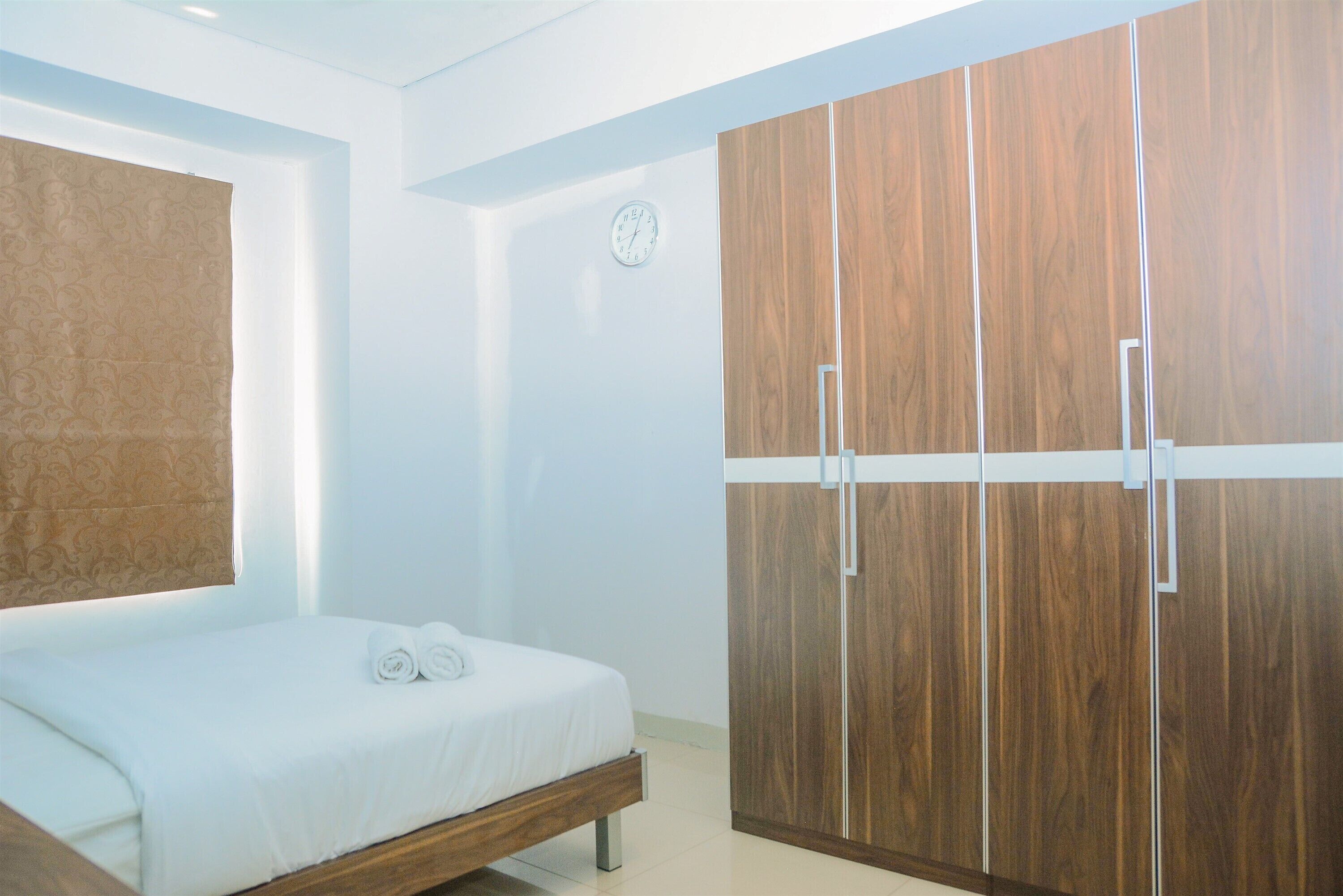 A bedroom with a bed, a wooden wardrobe, and a wall clock.