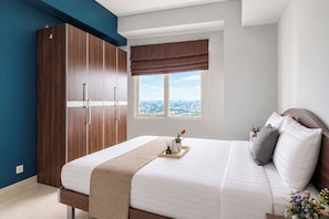 Un dormitorio con una cama grande, un armario, un ventanal con vistas y una mesita de noche con una bandeja.