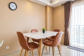 Un comedor moderno con una mesa blanca, cuatro sillas marrones, una pequeña planta en maceta y un reloj de pared.