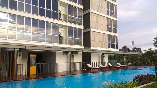 Un hotel moderno con piscina, varios balcones y un jardín bien cuidado.