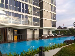 A modern hotel with a swimming pool, multiple balconies, and a well-maintained garden area.