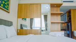 Una habitación de hotel con cama, armario, espejo, televisor y kitchenette.