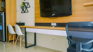 Un espacio de oficina moderno con un escritorio de madera, dos sillas blancas, una silla de oficina negra, un televisor de pantalla plana montado en la pared y una pequeña estantería con plantas.