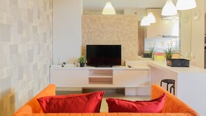 A modern living room with a flat-screen TV, orange sofas, and pendant lights. - Tranquil 2BR Apartment at Bintaro Park View (Jakarta)