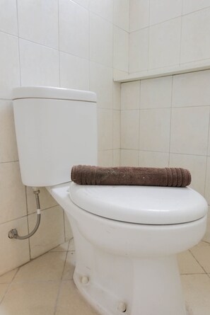 A white toilet with a brown towel on the seat, a visible pipe, and tiled walls.