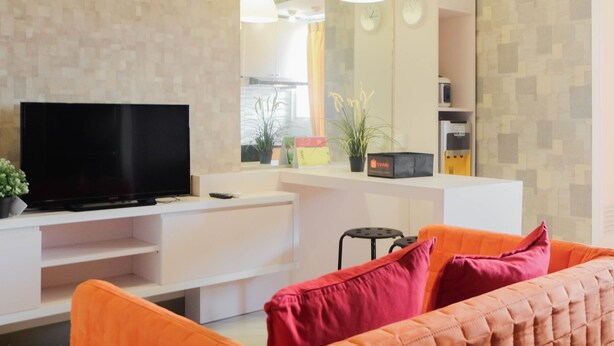 A modern living room with a flat-screen TV, orange sofa, and pendant lights. - Tranquil 2BR Apartment at Bintaro Park View (Jakarta)