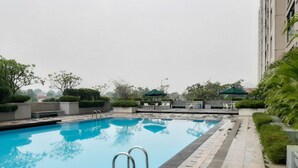 A rooftop swimming pool with a clear blue water surface, surrounded by greenery and modern outdoor furniture. - Tranquil 2BR Apartment at Bintaro Park View (Jakarta)