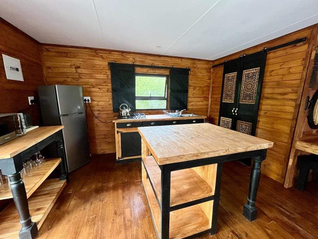 A compact kitchen with wooden walls, a refrigerator, a sink, and a wooden table.