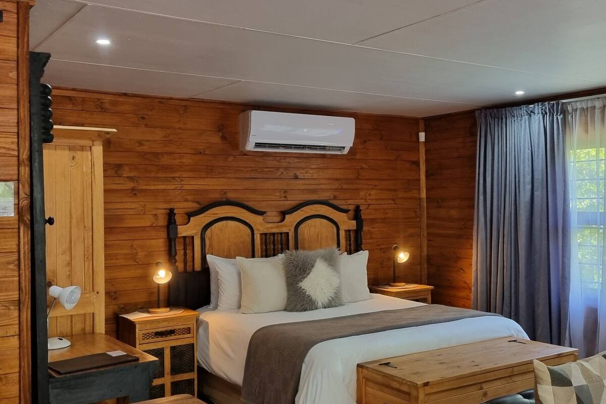 A wooden-paneled room with a bed, bedside lamps, a nightstand, and a window with curtains.