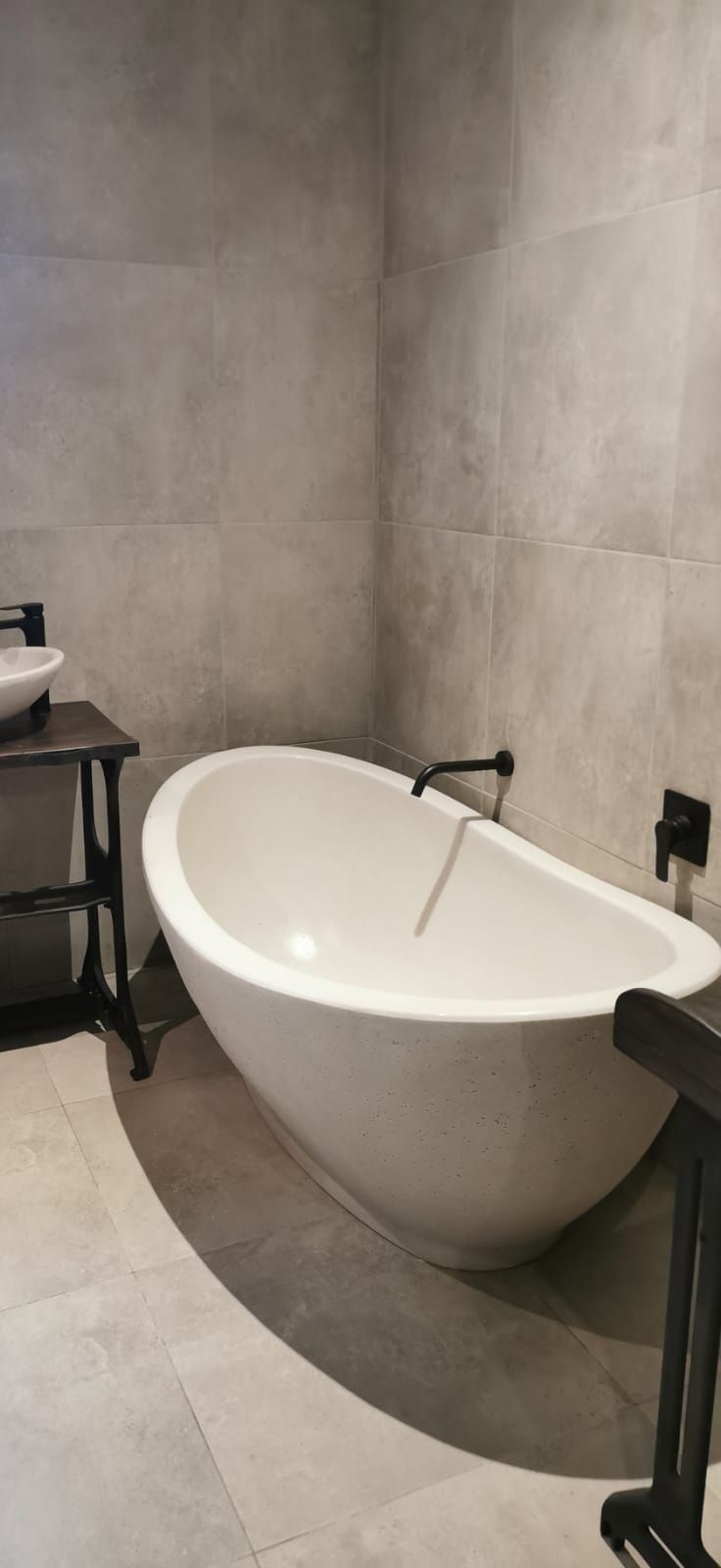 Un baño moderno con una bañera independiente, un lavabo negro y un grifo negro.