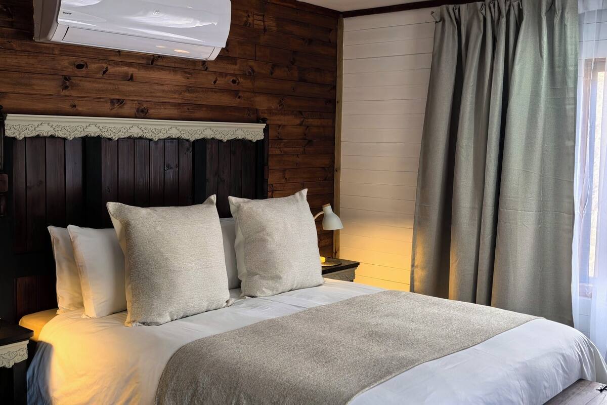 A bedroom with a wooden headboard, a bed with white bedding, two bedside lamps, and a window with curtains.