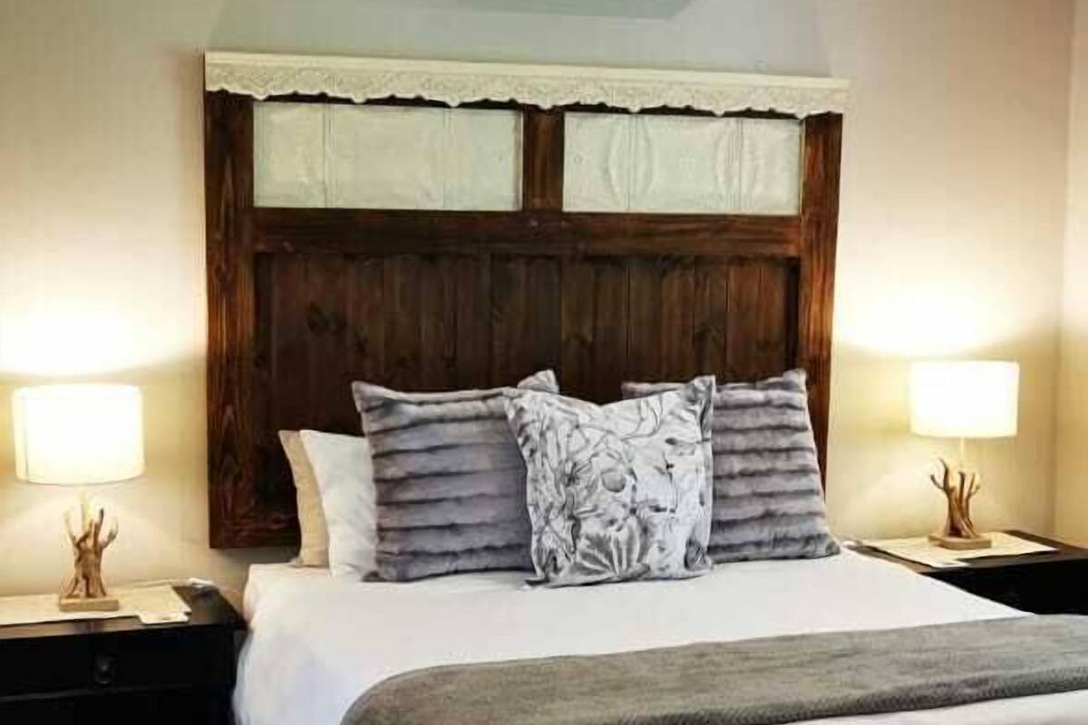 A neatly made bed with a wooden headboard, two bedside lamps, and a patterned throw blanket.